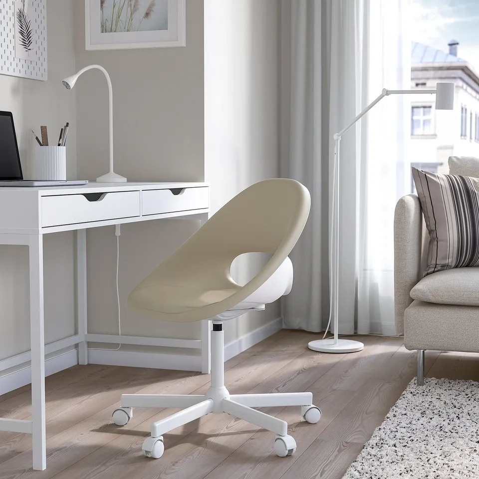 Modern home office: white ELDBERGET chair, desk, grey sofa, laptop, lamp, artwork, large window, rug.