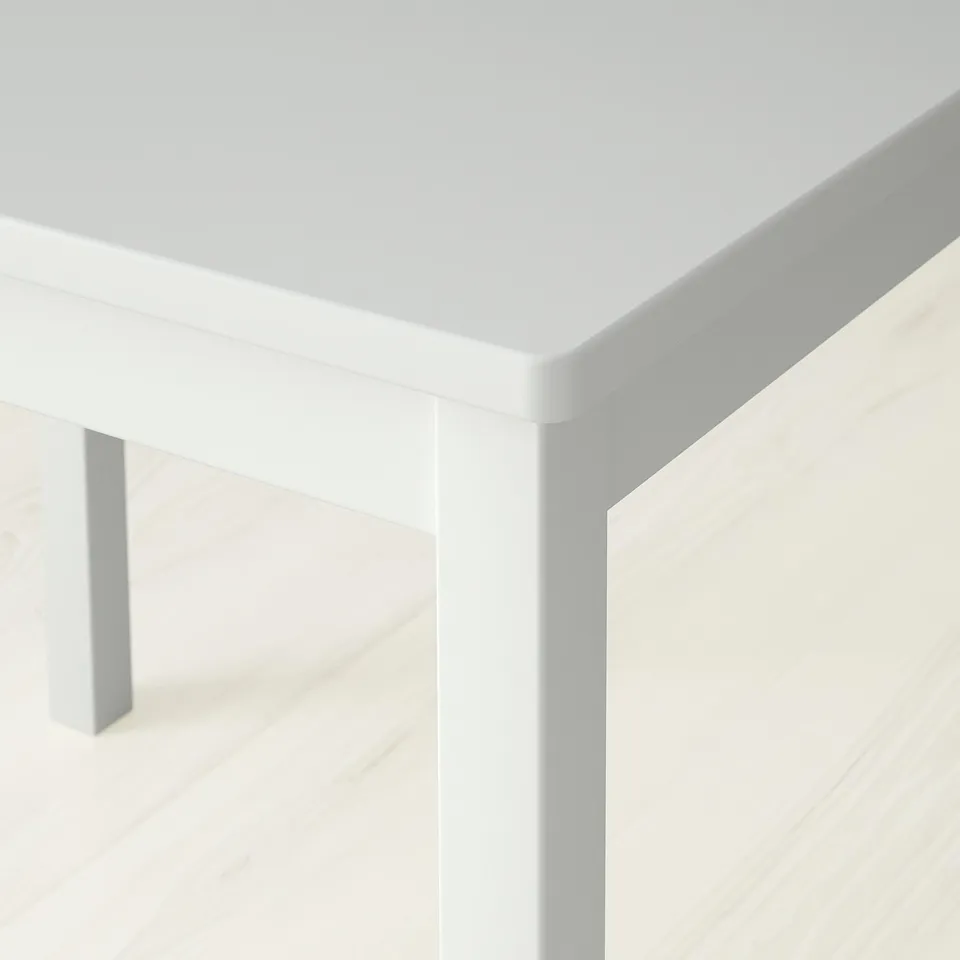 Clean-lined childrens table, sleek white surface, sturdy wooden legs.