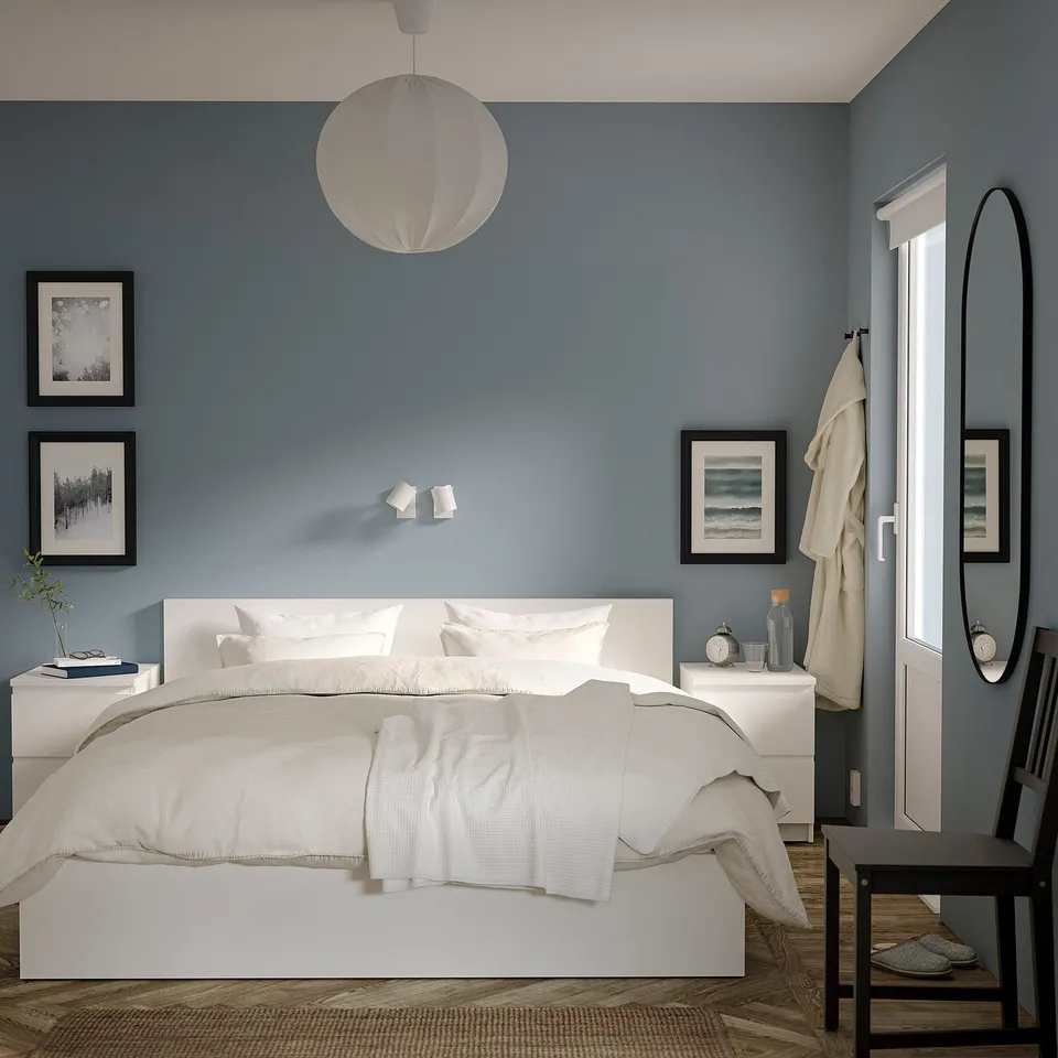 Blue bedroom with MALM bed, nightstands, and hanging light. Clean lines, white bedding, round mirror, art, and robe.