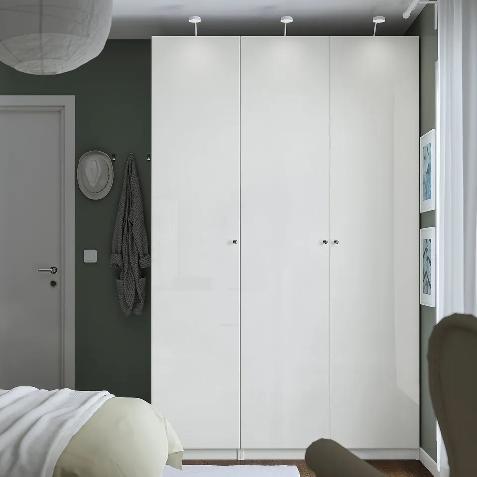 Modern bedroom with tall white PAX wardrobe, sleek handles, integrated lighting, green wall, and minimalist design.