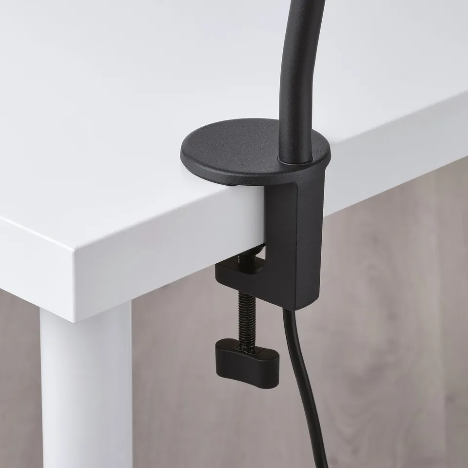 Modern black clamp lamp mounted on white desk edge, showcasing its sleek design and adjustable arm.