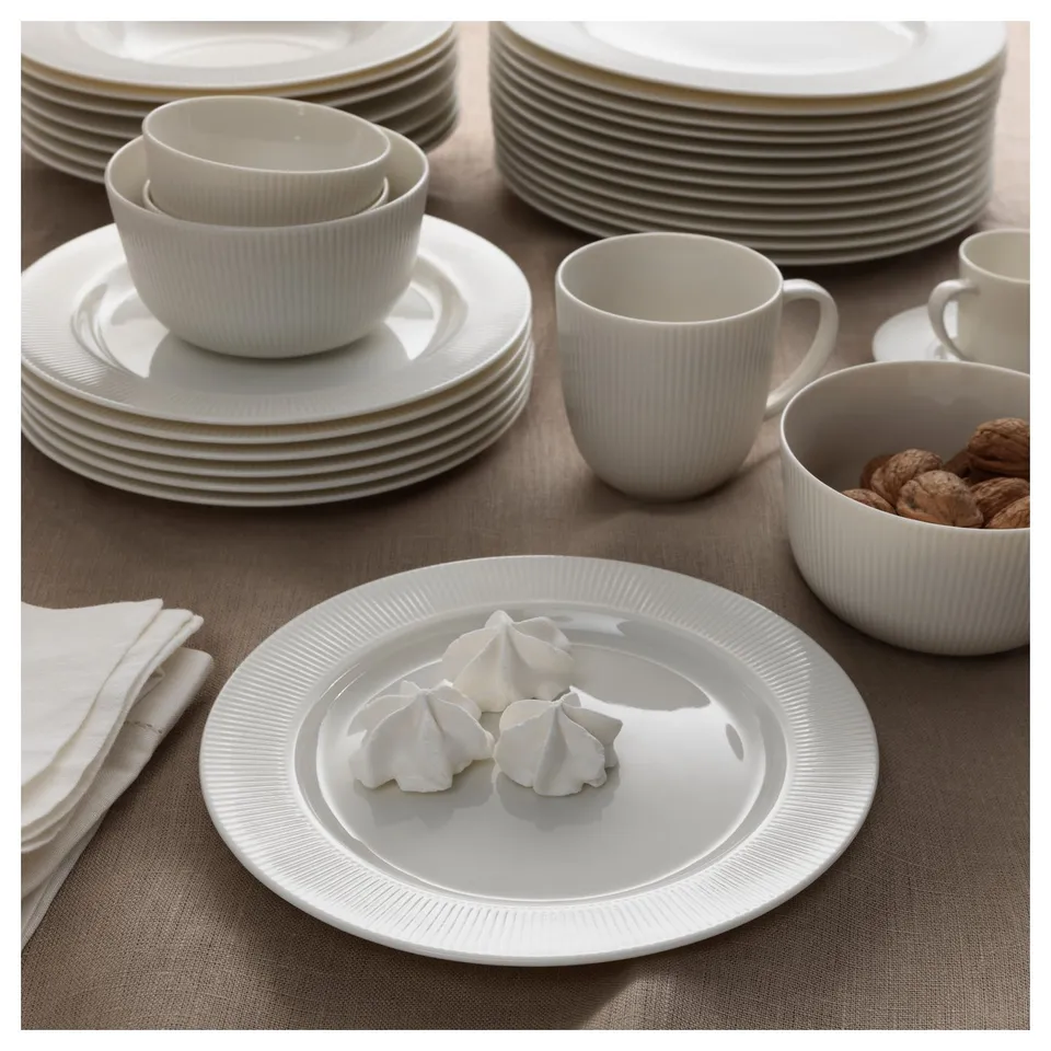White porcelain dinner set, including plates and cups, arranged neatly on a brown tablecloth. One plate three meringue cookies.