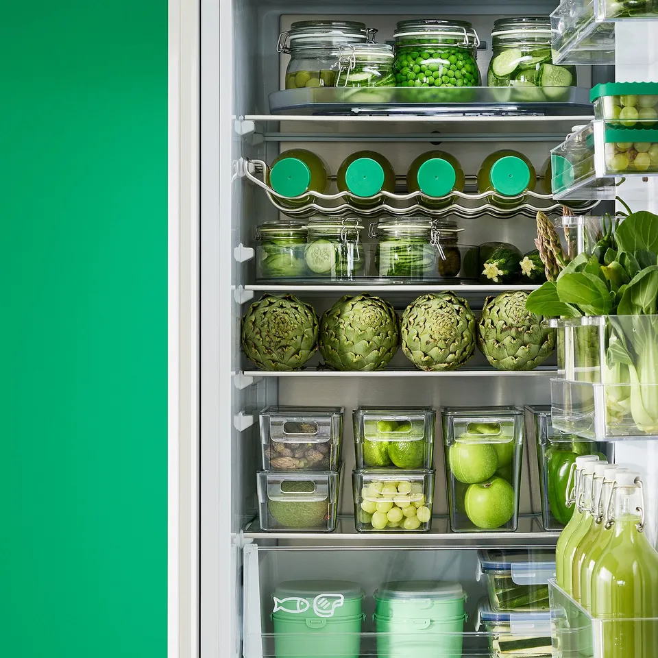 A well-organized fridge with clear, stackable storage boxes, each with lids for freshness, holding various fruits and vegetables neatly.