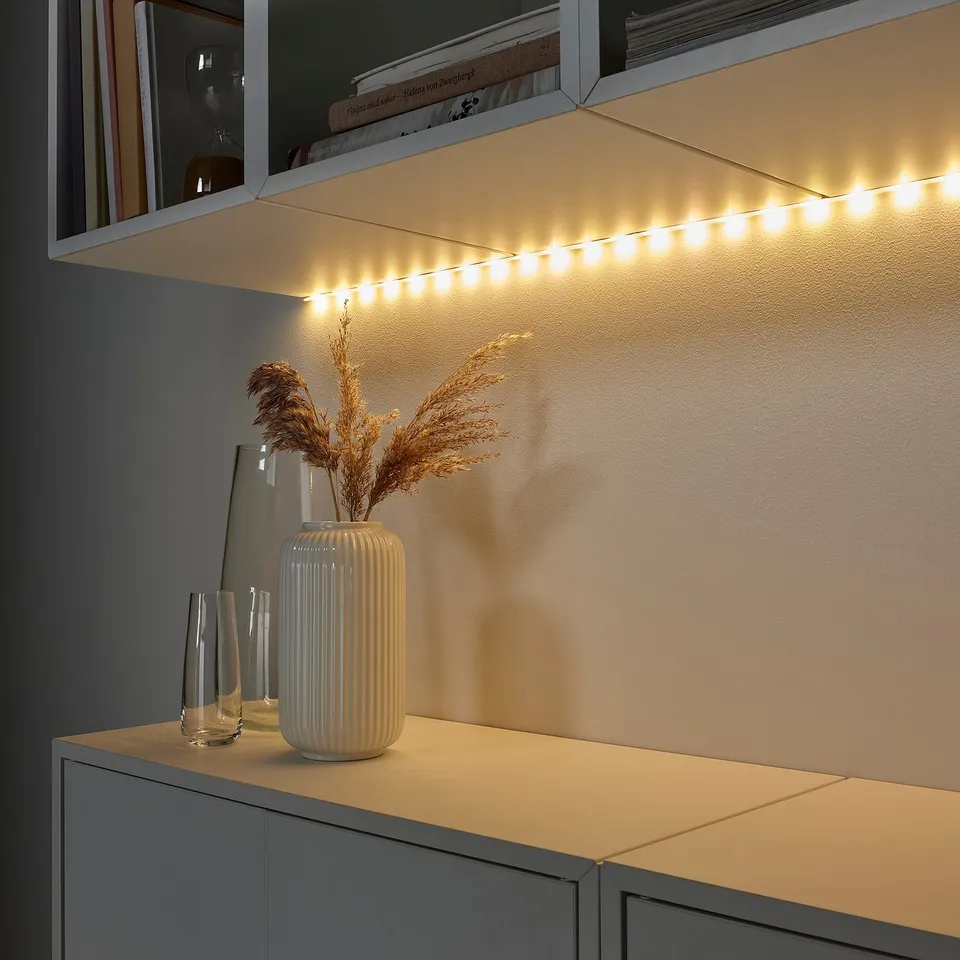 Under-shelf led lights illuminate a decorative vase and dried flowers on a cabinet.