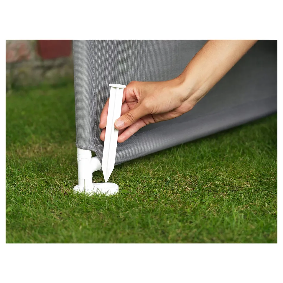 Hand placing white plastic stake into grassy area against grey mesh structure.