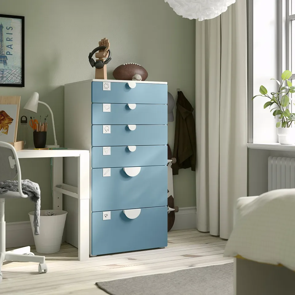 Blue SMÅSTAD chest with 5 labelled drawers, decor on top, near window with curtains and desk.