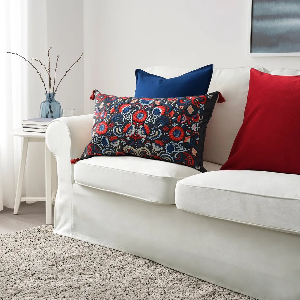 White sofa with colourful pillows, SKOGSKORN navy floral cushion, red & navy pillows, blue vase with branches, cosy and vibrant.