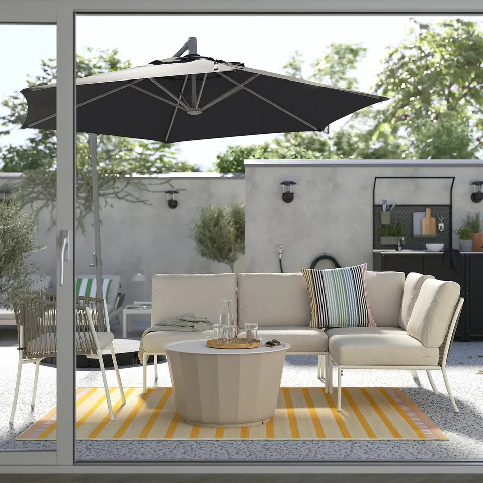 Modern outdoor patio with white sectional sofa, striped rug, round table, and black umbrella.