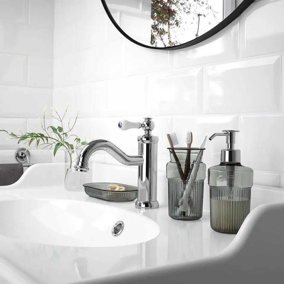 Modern bathroom featuring BROFJÄRDEN accessories: shiny chrome tap, green soap dispenser & cup next to a white sink.