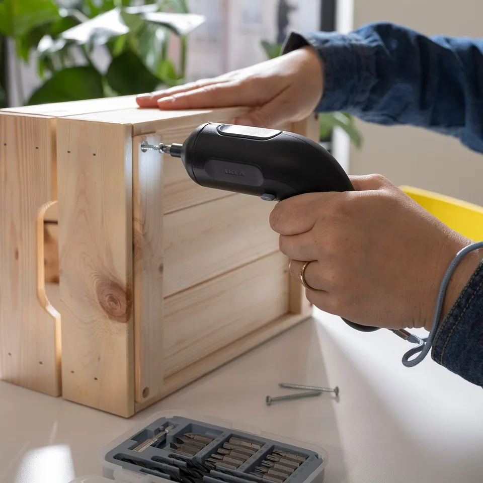 A person is using a TRIXIG cordless screwdriver with a built-in led light to assemble wooden furniture, held by its ergonomic rubber grip.