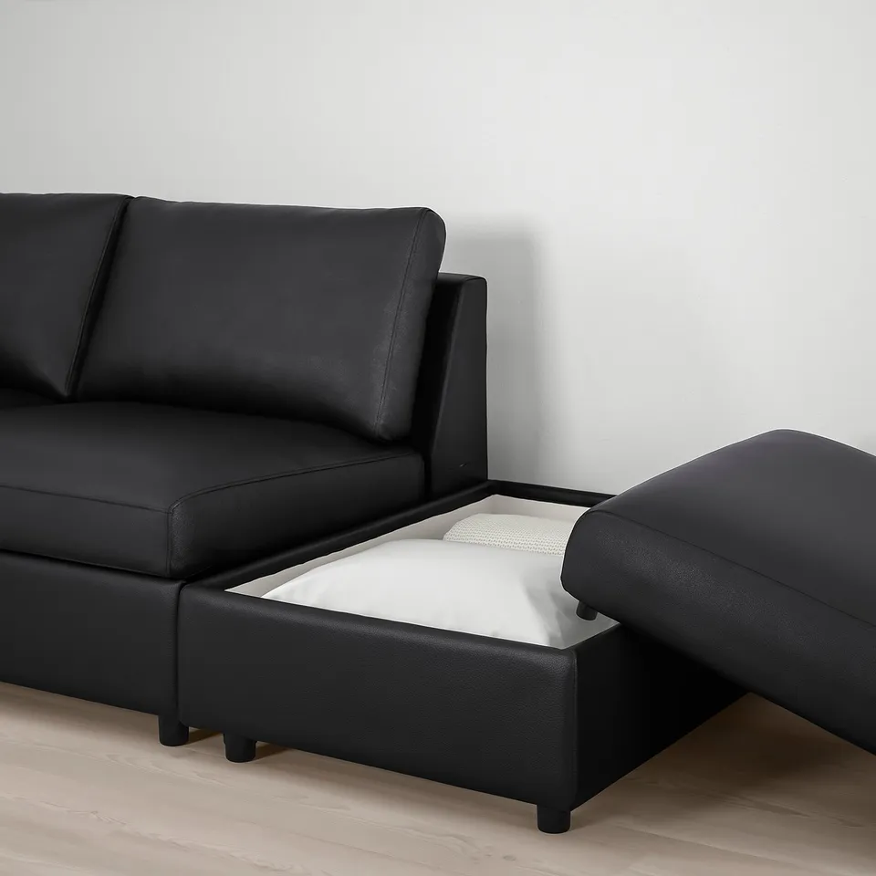 Black leather couch with storage compartment open, revealing white folded item inside.
