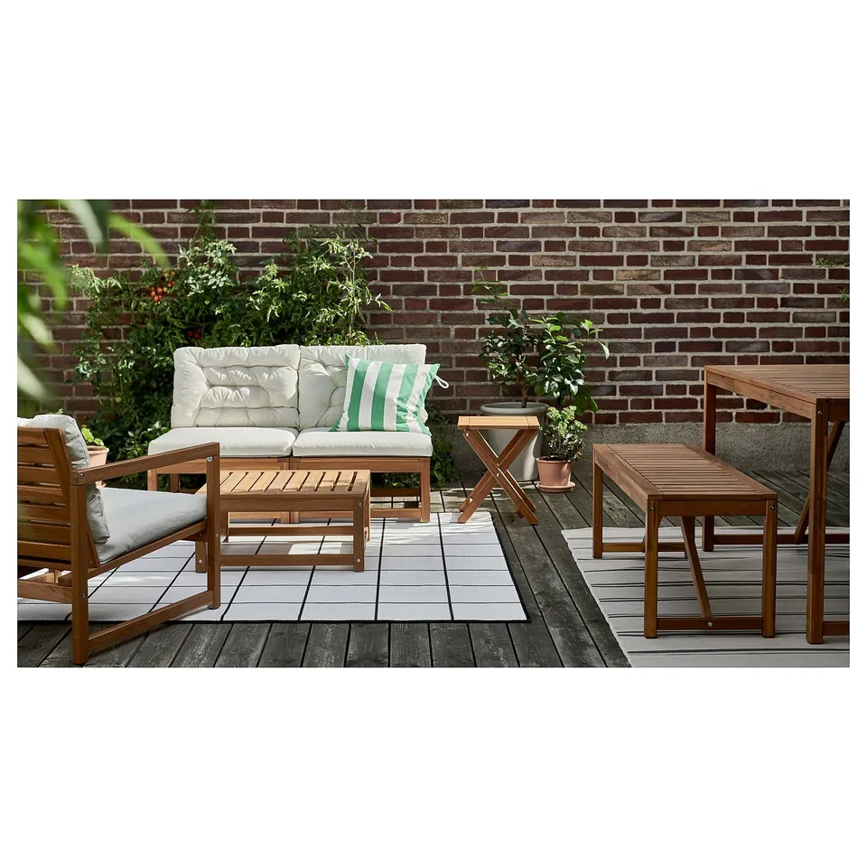 Outdoor patio set: includes sofa, chairs, and table. Crafted from acacia wood, light grey cushions, green striped pillow, against brick wall backdrop.