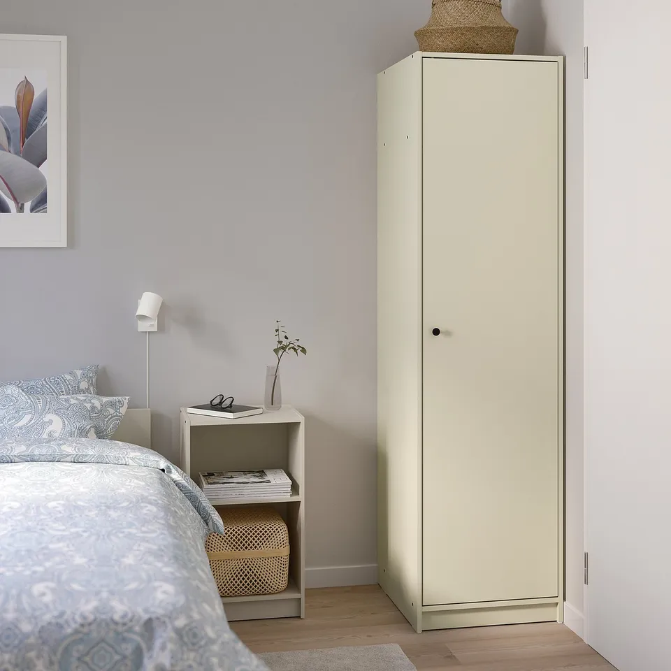 A GURSKEN tall, beige wardrobe beside a bed, featuring clean lines and useful storage.