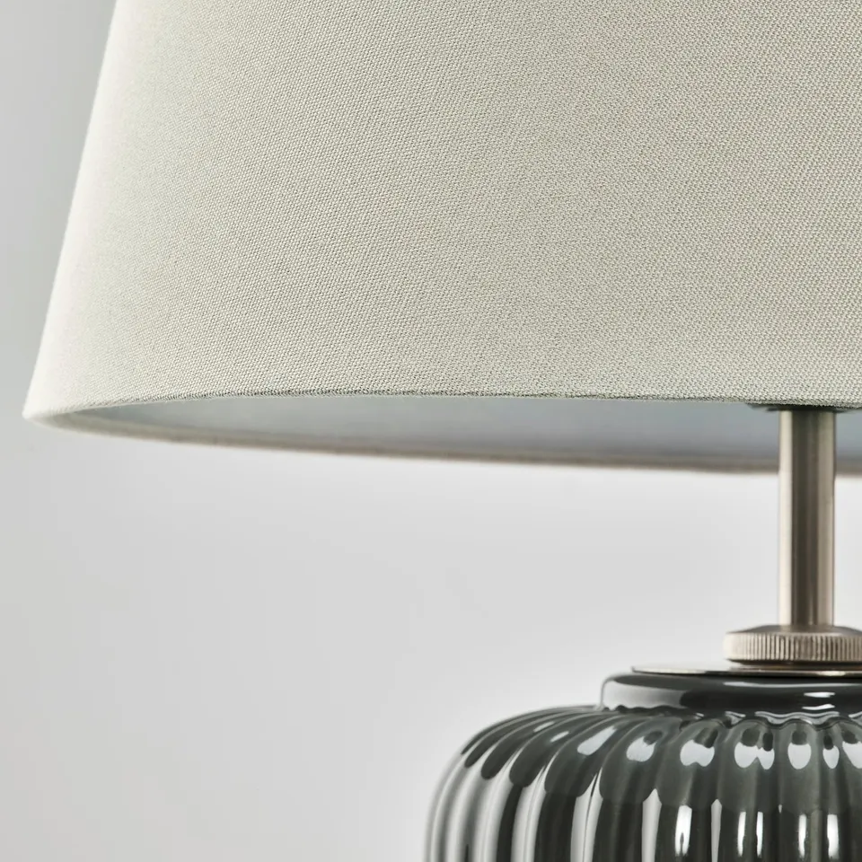 Grey lampshade with warm light on black base.