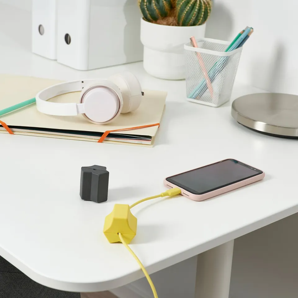 White desk with charging phone, headphones, notebooks, plant, pen holder.