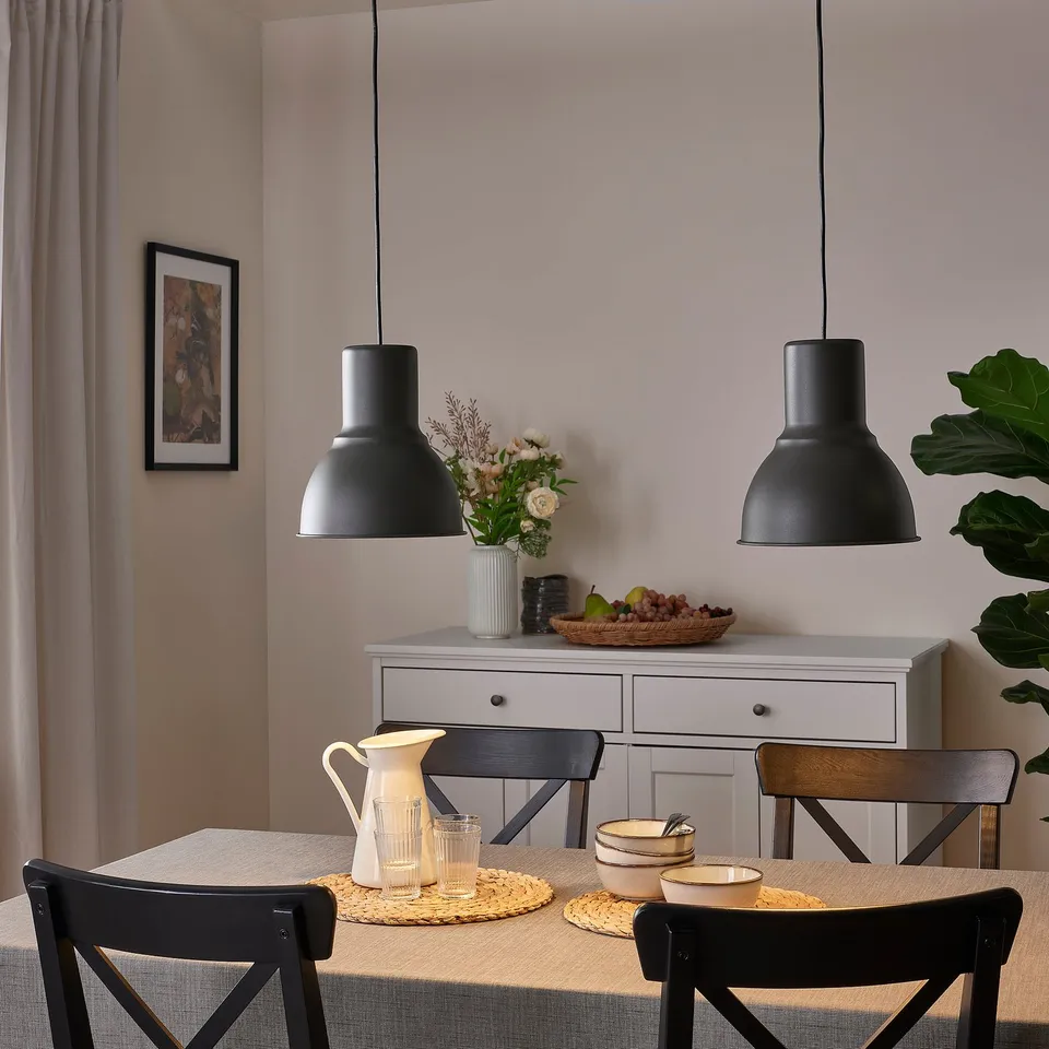 Black pendant lamps over dining table with chairs, casting light on tableware, flowers, and art.