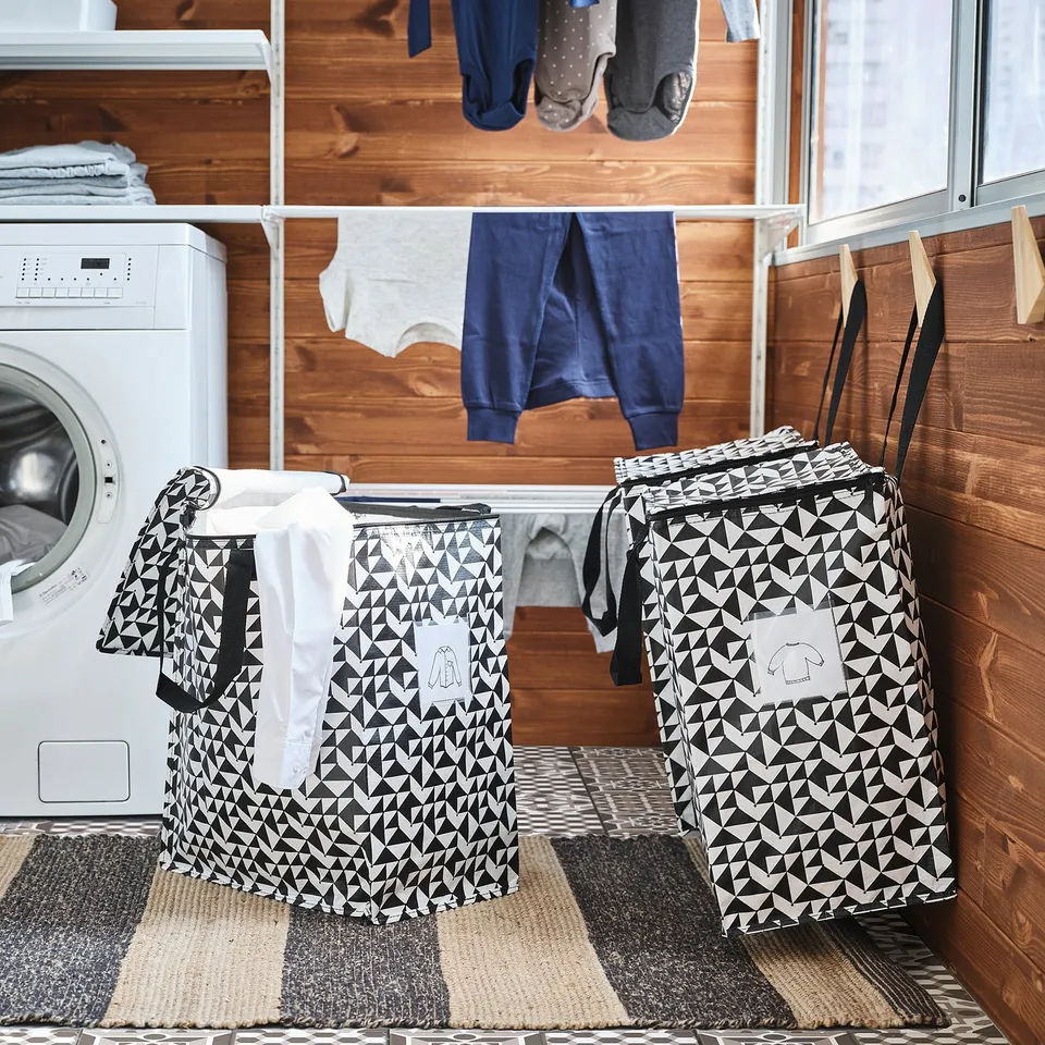 Laundry room with KNALLA bags, one with laundry, washing machine, and drying rack.