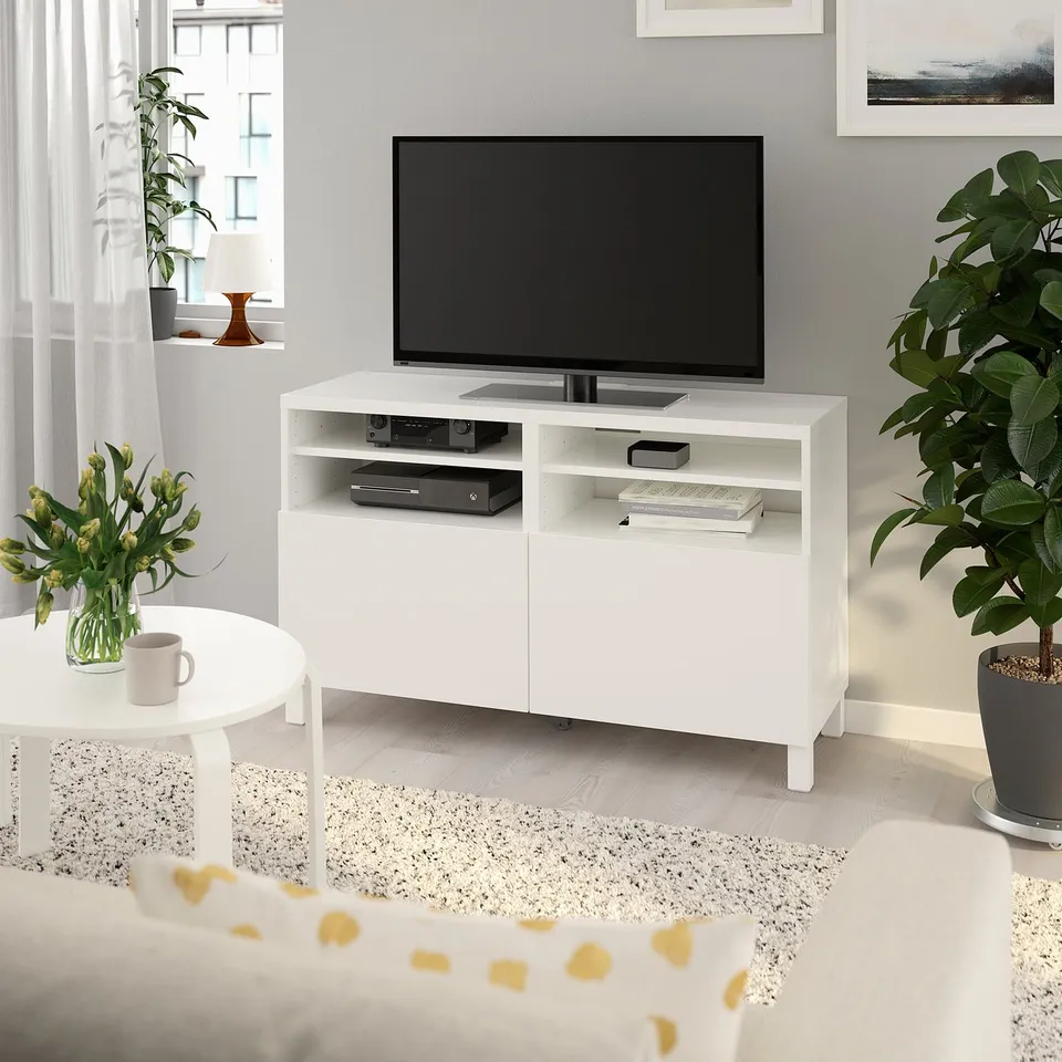 White BESTÅ tv stand with flat-screen tv, adjustable shelves, electronics, vase, plant, wall picture.
