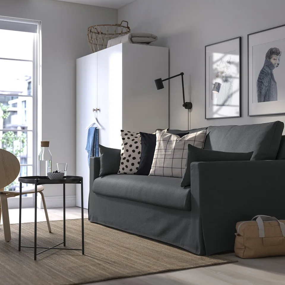 Modern living room with grey sofa, patterned cushions, art, side table, bright window, white cabinet.