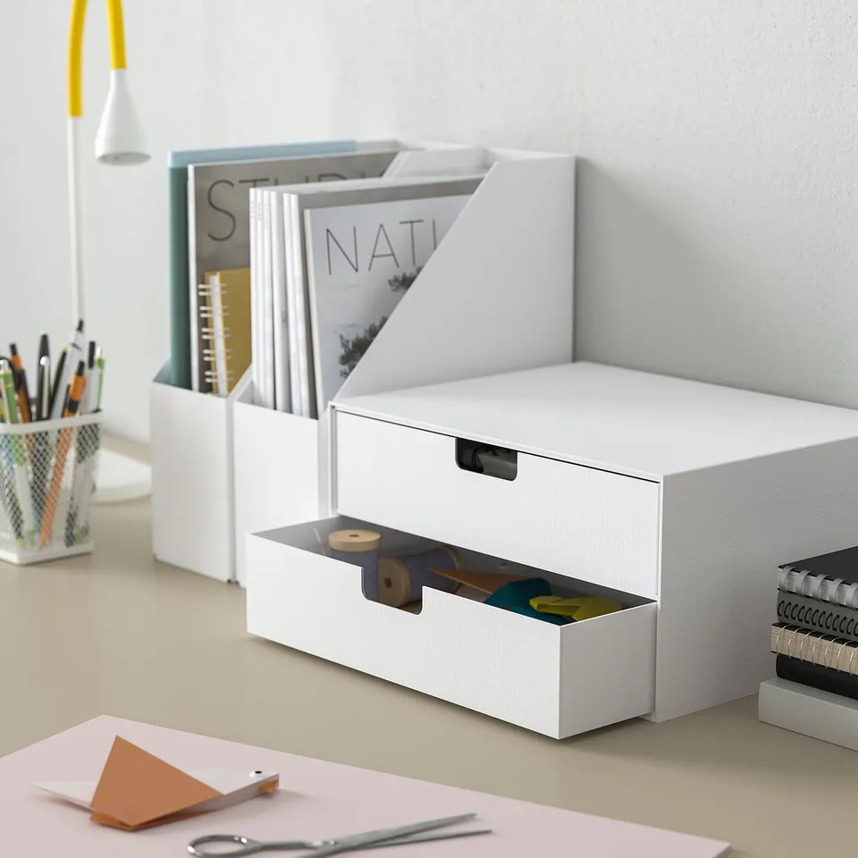 White mini chest on desk, holding stationery, among office supplies. Magazine and books in background.