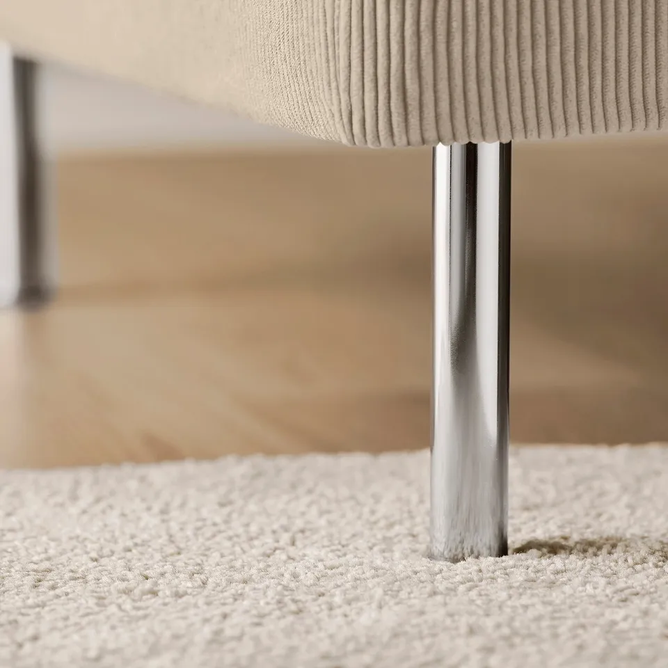 Modern sofa detail: plush, ribbed fabric seat, polished metal legs on soft carpet.
