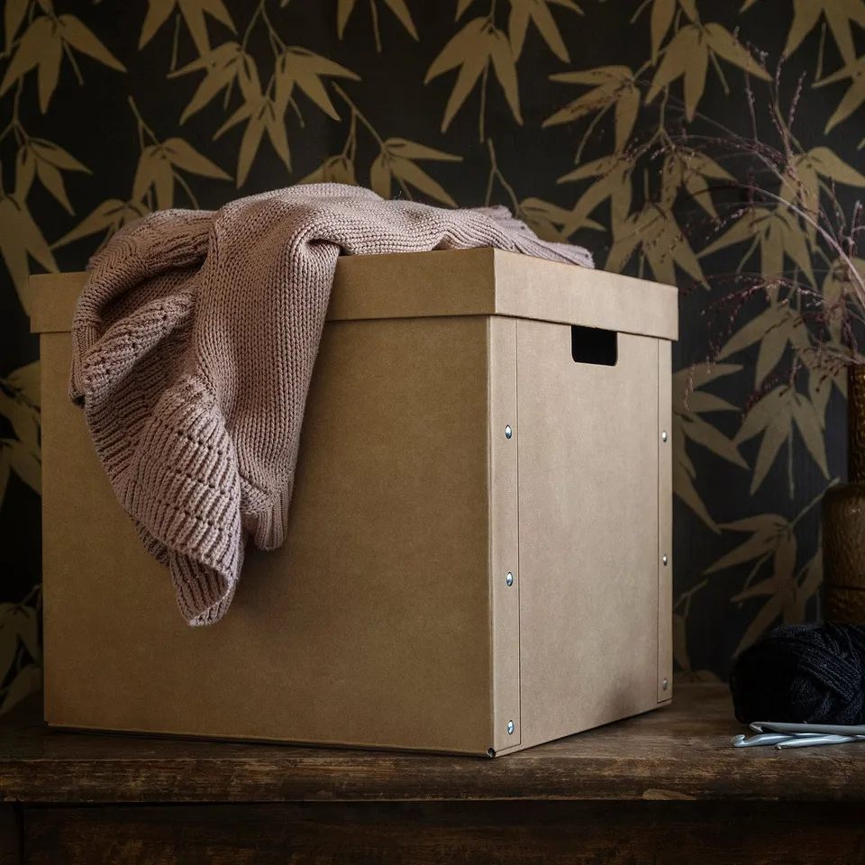 Cardboard box with blanket on shelf.