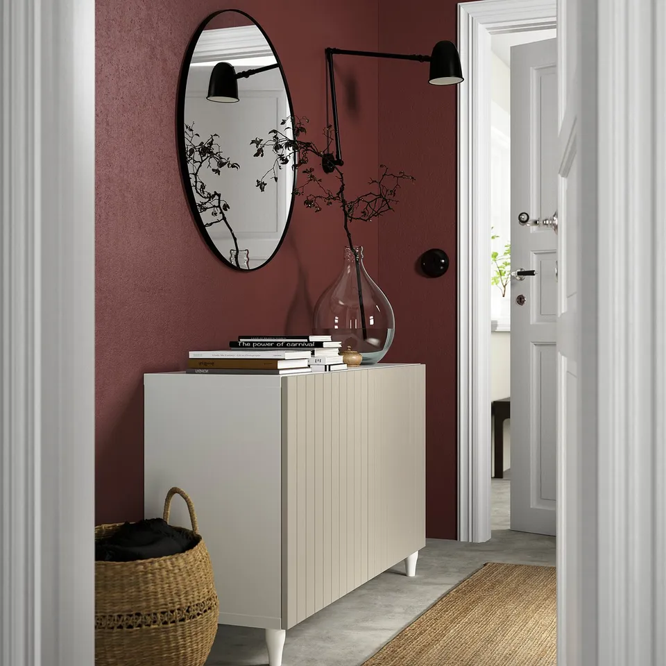 Modern entryway with maroon wall, white KABBARP legs under console, round mirror, black sconce, woven basket.