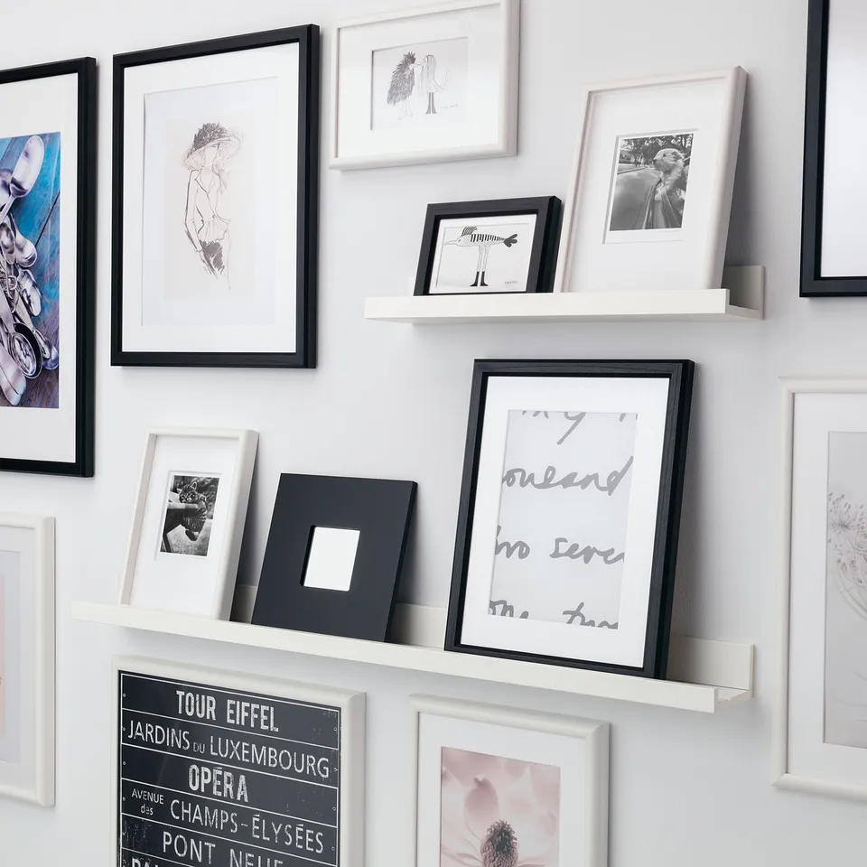 A wall-mounted shelf displays various framed photos in a gallery style. The shelfs groove securely holds smaller frames upright.