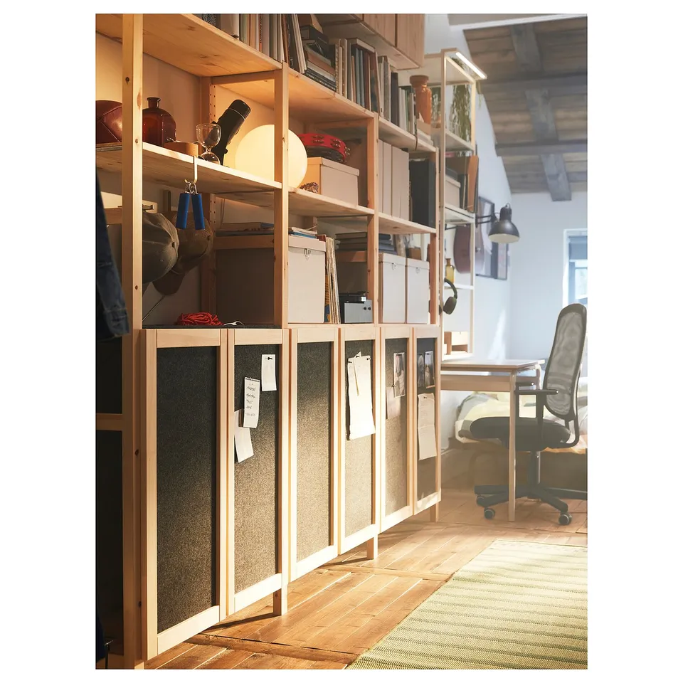 Home office with IVAR storage. Wooden shelves hold books and boxes. Desk with chair. Felt-covered doors.