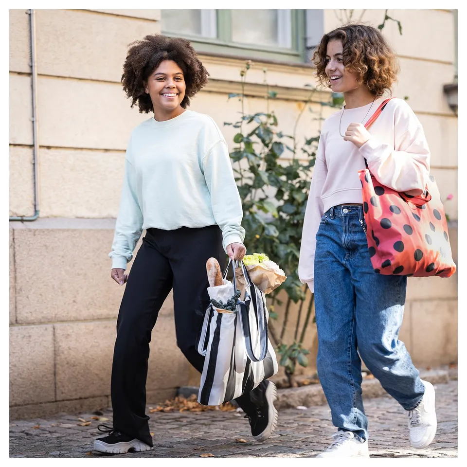 Two people smile, walking outdoors with shopping bags.