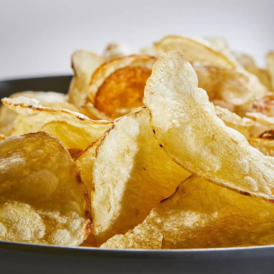 Black bowl filled with golden potato crisps, slightly overlapping, perfect for snacking.