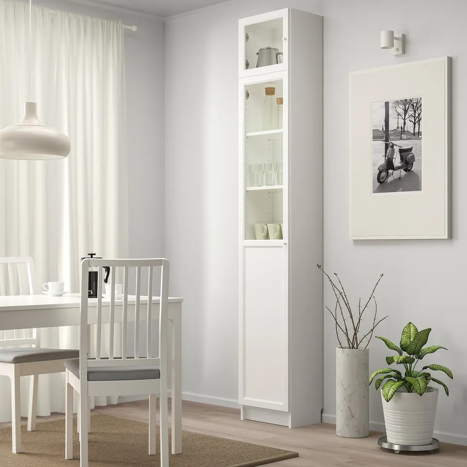 Modern dining area with BILLY cabinet, chairs, and window. Vintage scooter, plant, and marble vase. Tall cabinet for storage.