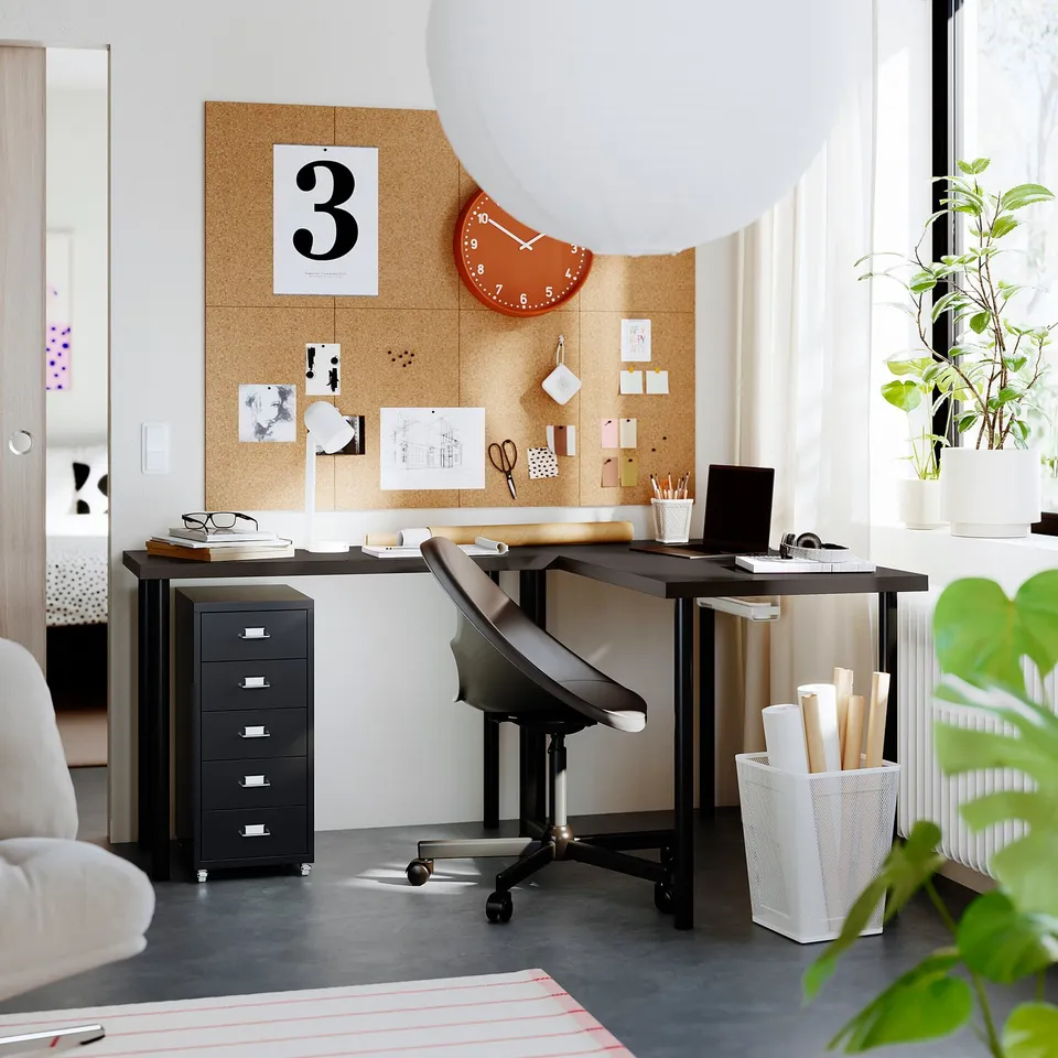 Home office with black LAGKAPTEN desk, chair, and corkboard with clock, plants, and storage units.