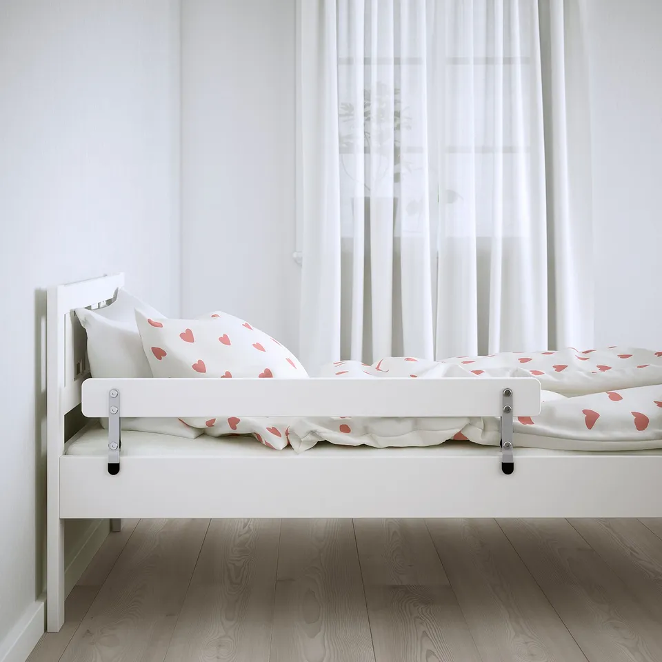 A white junior bed with heart-patterned bedding and a safety guardrail on both sides.