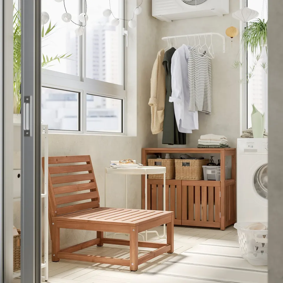 Modern balcony with NÄMMARÖ wooden chair, table, and storage. Clothes hang nearby.