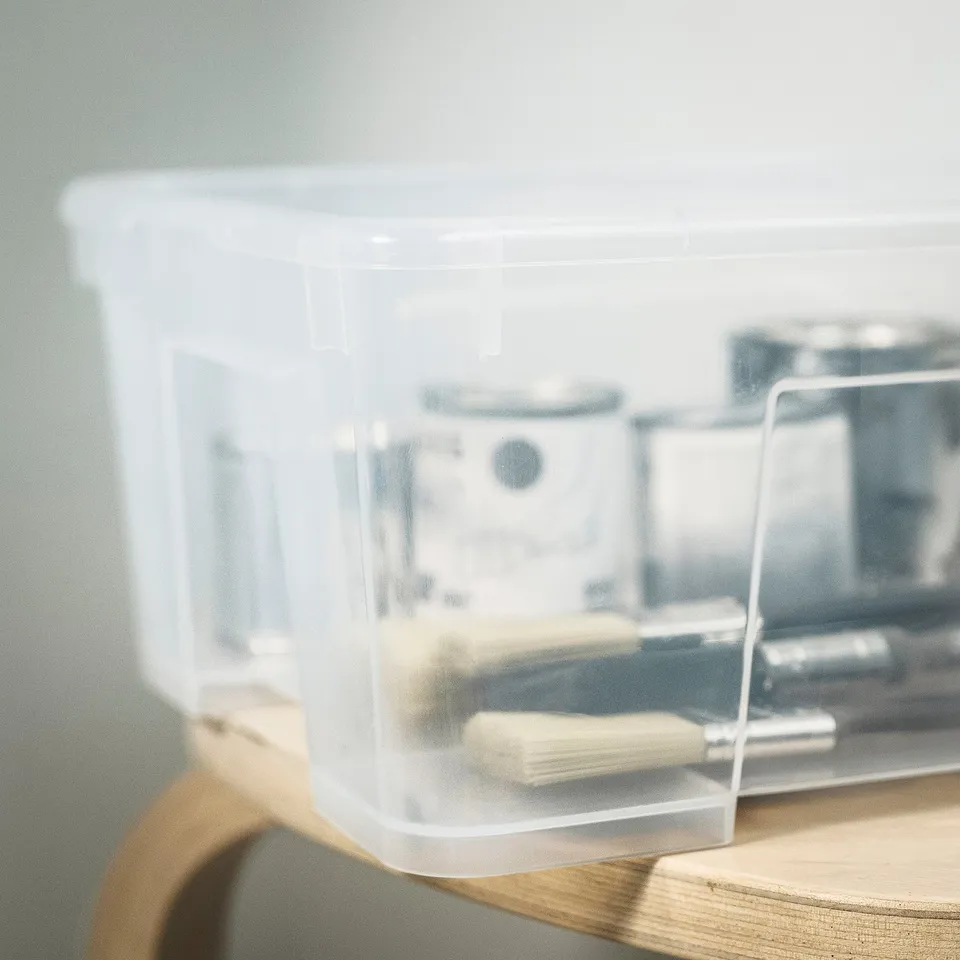 Clear plastic storage bin holding organising tools on wooden shelf.