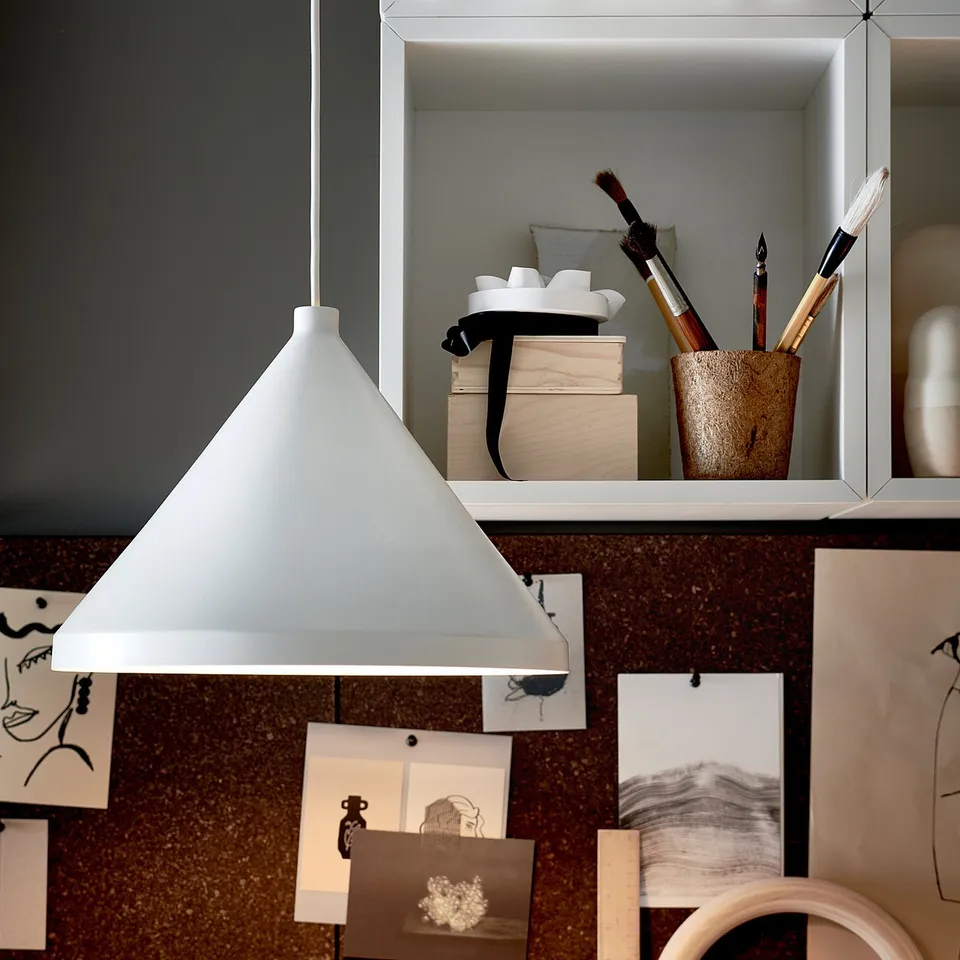 White EKET storage cabinet with various art supplies and sketches, hanging light, and dark green wall.
