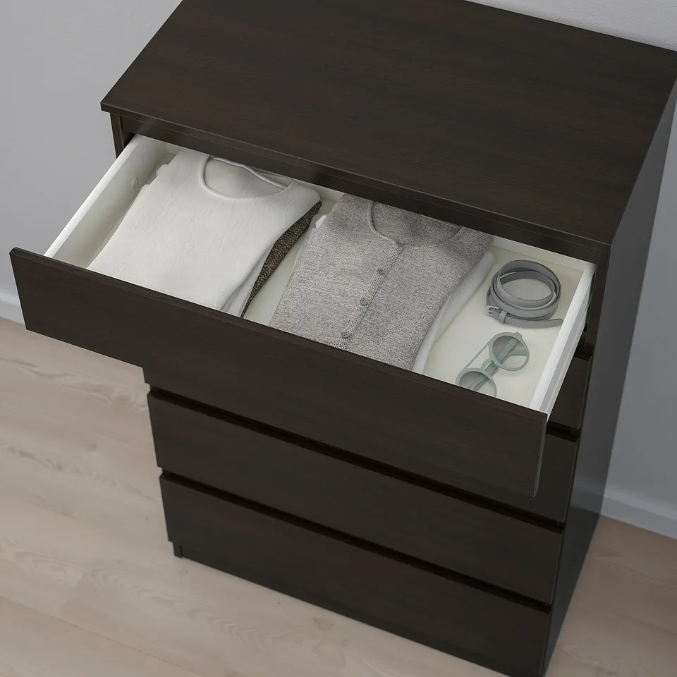 Dark wooden chest of drawers with one open drawer showing neatly folded clothes and accessories.