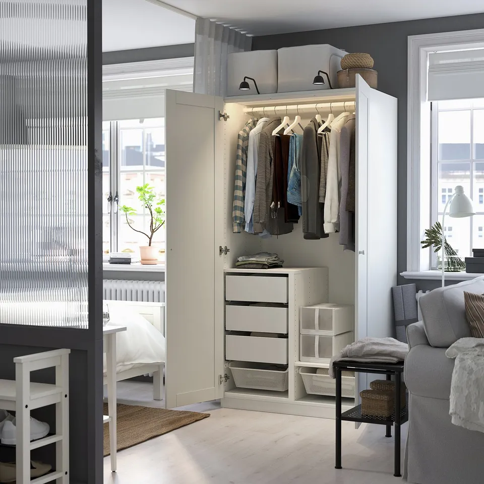 Open white PAX wardrobe displaying clothes, drawers, and interior organisation under soft lighting.