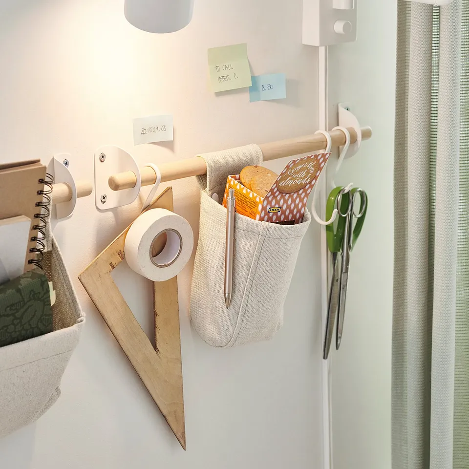 Organised wall rack with laminate hooks and fabric pouches for pens, scissors, and notes. White, metal and fabric. Practical and space-saving.
