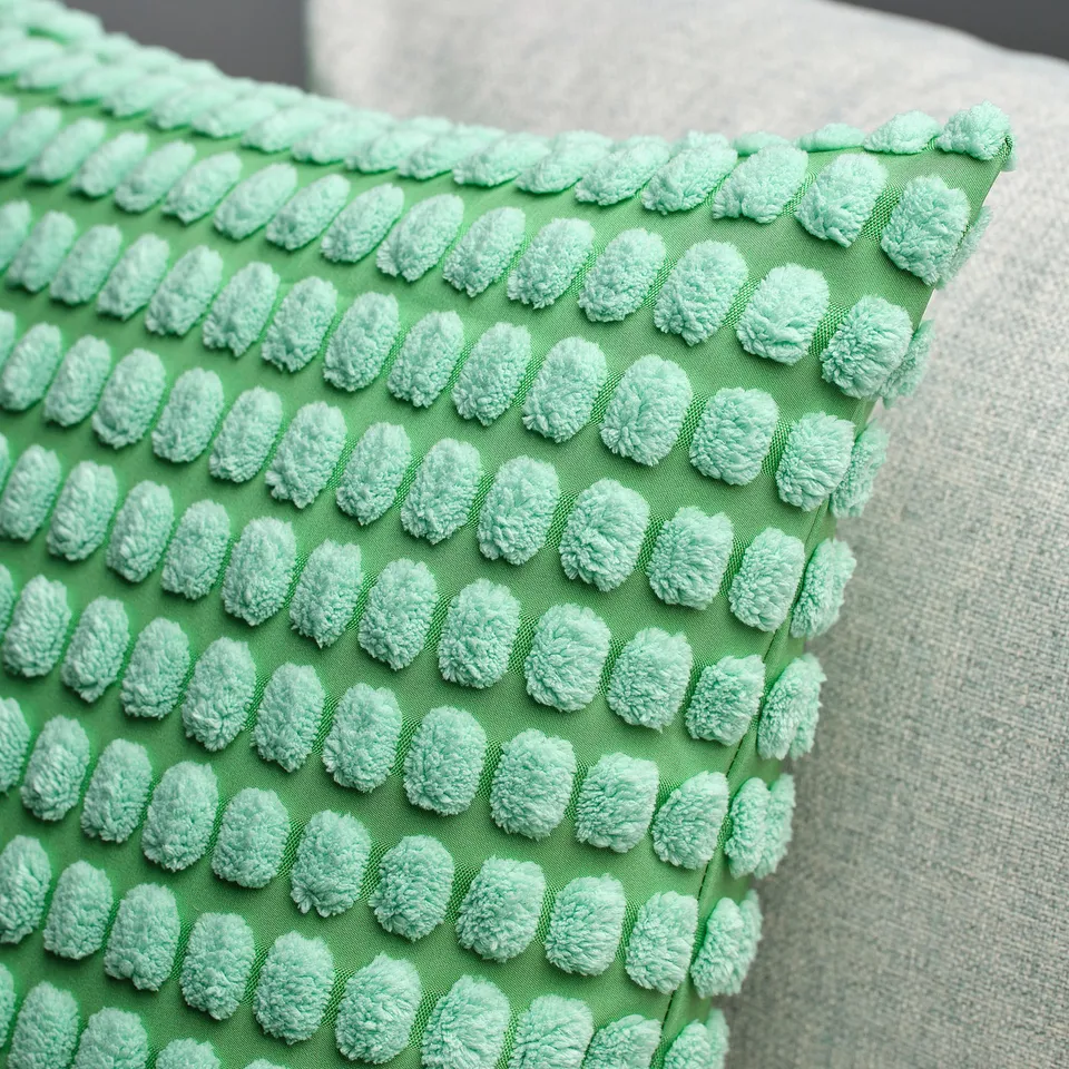 Close-up of soft, textured green pillow on bed, detailed with small tufted circles, quality fabric.