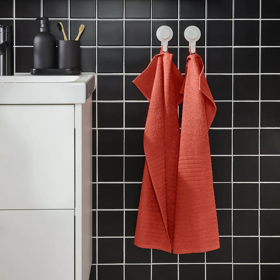 Red VÅGSJÖN towels hang on bathroom wall hooks against black tiles.