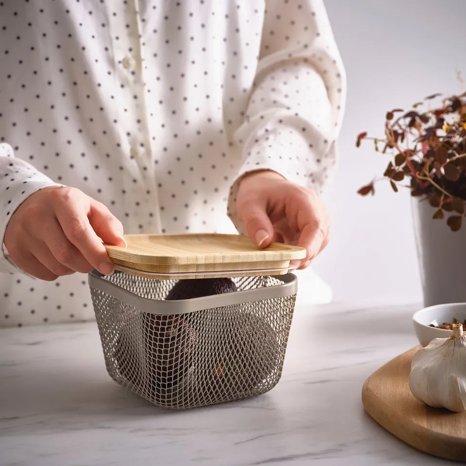 A person opens an IKEA 365+ mesh food storage basket with lid, showcasing its design for air circulation and visibility.