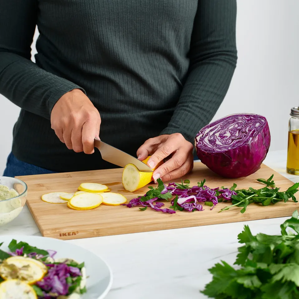 Person slicing lemon on bamboo cutting board with chopped veggies. Ikea APTITLIG board shown.