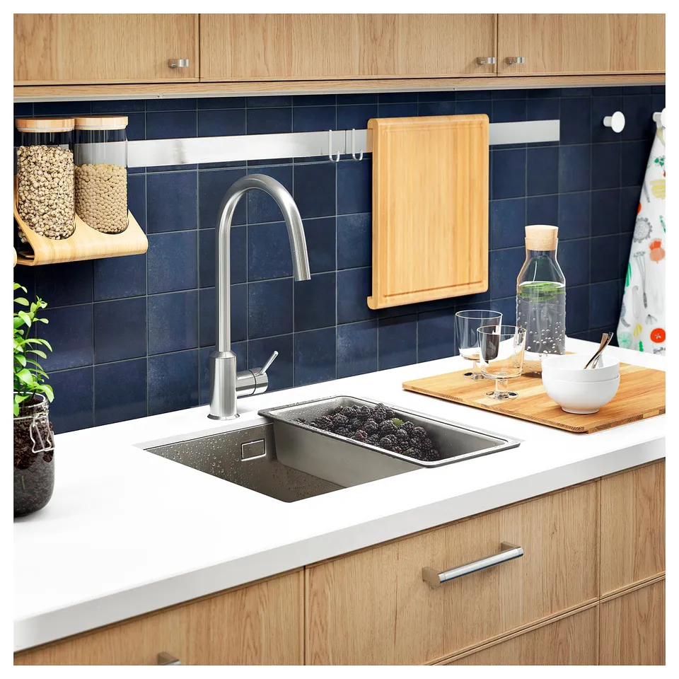 Modern kitchen sink, dark blue tiles, wood cabinets, silver tap. Colander with blackberries, cutting board on counter.