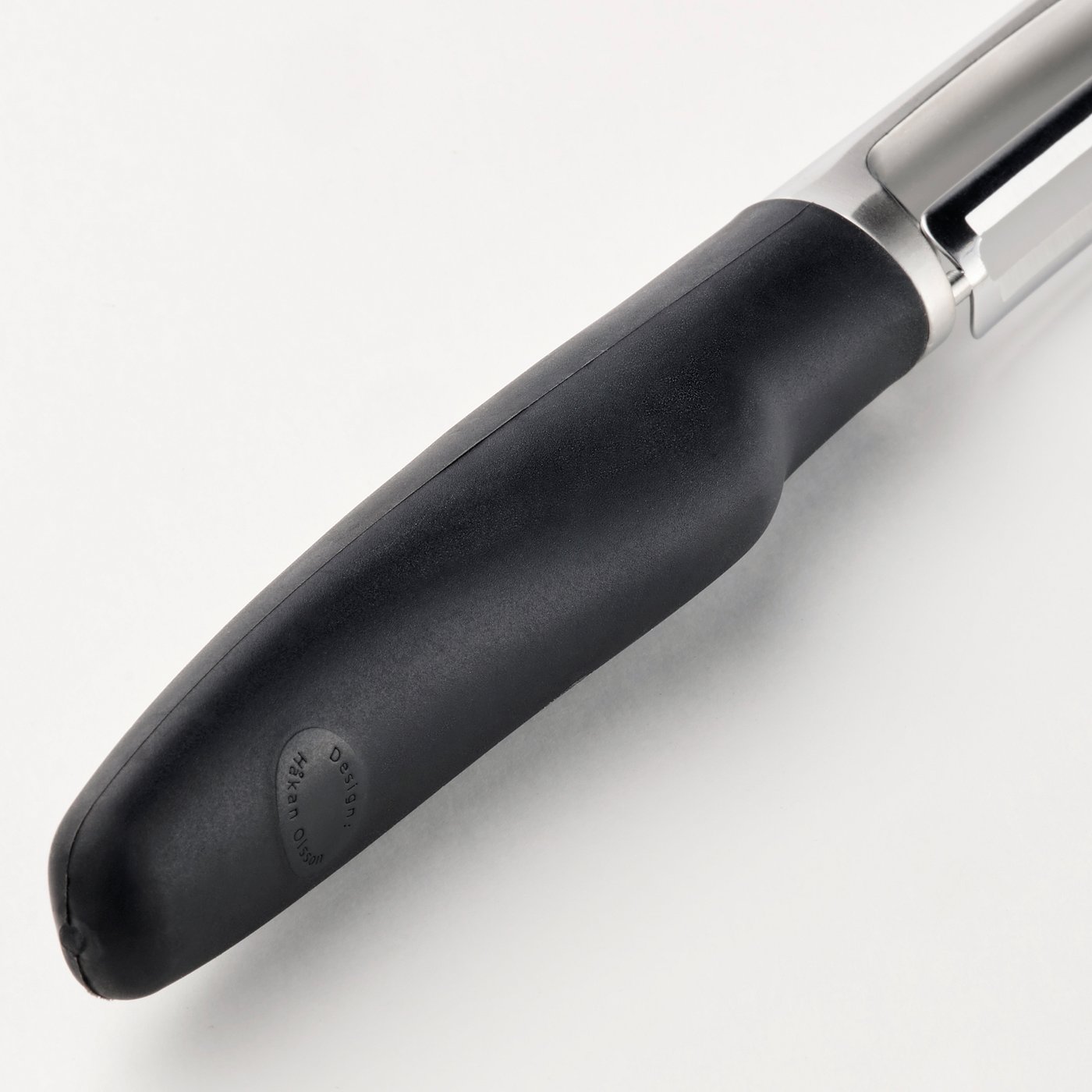 Peeler with black grip and metallic body rests on surface. Firm grip and sharp stainless steel blade.