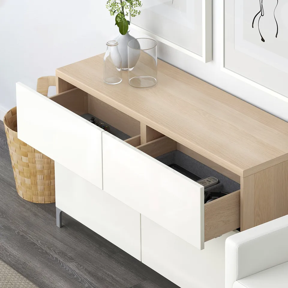 Wooden unit with open drawer showing remote, white vases, and basket on floor. Integrated storage for tv accessories.