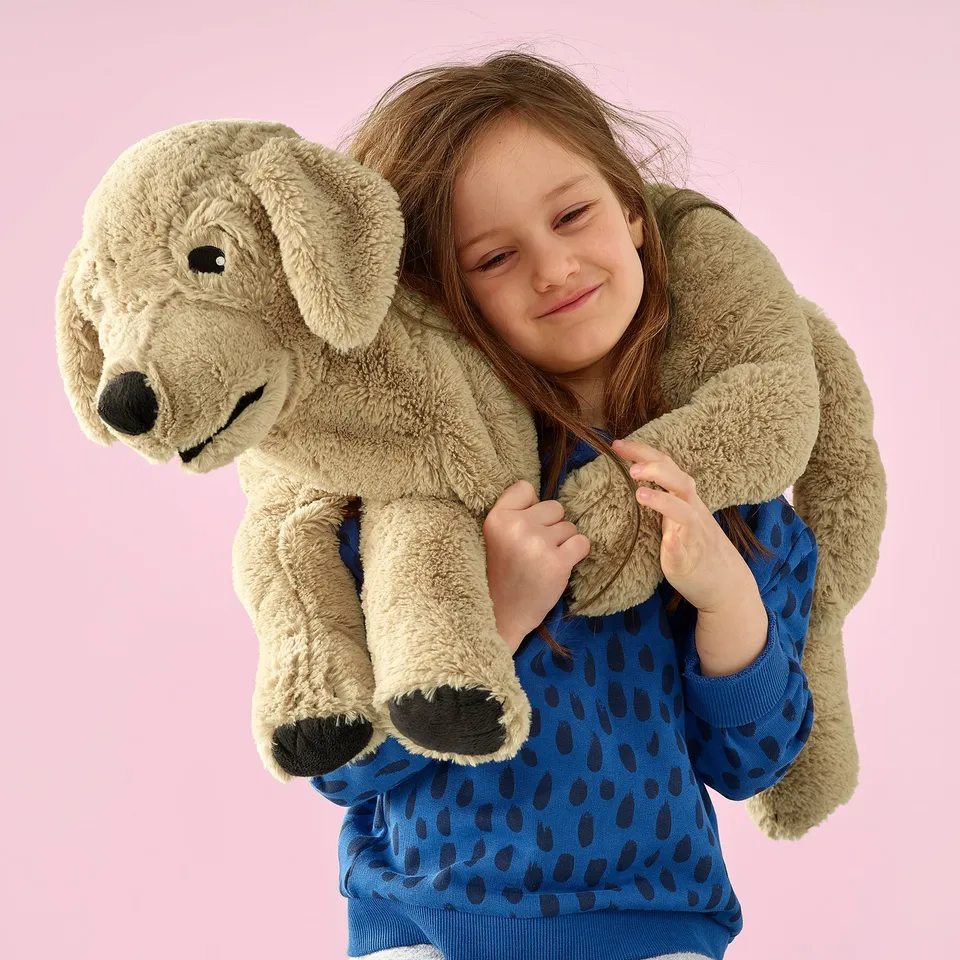 A girl in blue pyjamas holds a large stuffed dog toy; its soft, huggable, and ready for play or cuddling.
