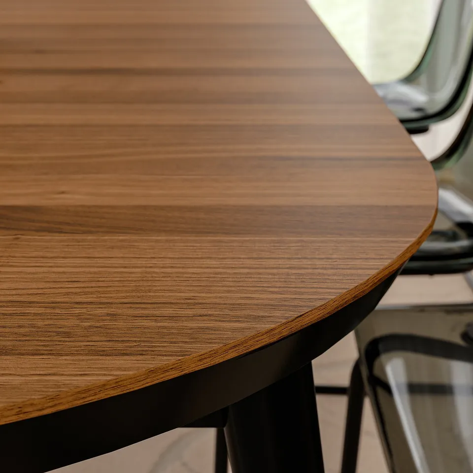 Round wooden table close-up, showing polished, natural grain wood top with sleek, black metal edge support.