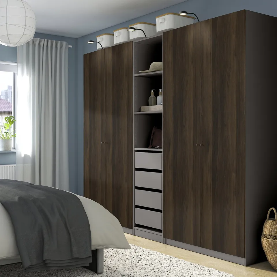 Modern bedroom large dark wood PAX wardrobe, taller than bed, with open shelves and drawers. Light blue walls, white curtains, and cosy bedding.